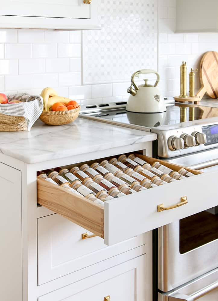white kitchen with open organized spice drawer, glass jars with minimalist labels, Carrara marble countertops