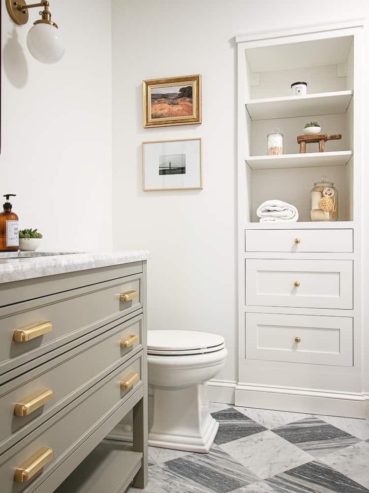 small basement bathroom with white walls, marble checkerboard floors, gray vanity, builtin shelves