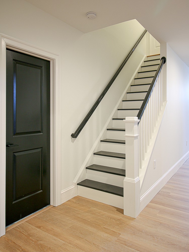 basement with white walls and black interior door, stairs painted black, lvp floors